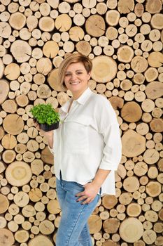 Beautiful young woman holding a micro-green color on the background of a wooden log wall.