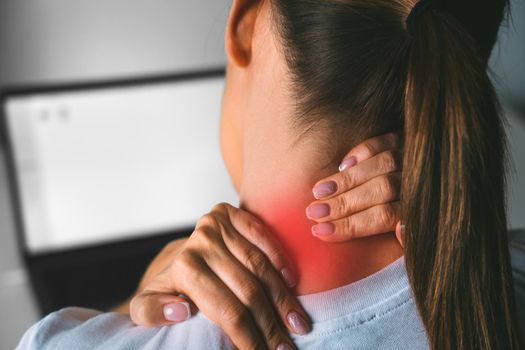 Neck pain after working on computer. Young woman massaging neck to relieve pain after working on pc. High quality photo