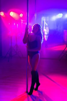 Pole dance. Young slender sexy woman dancing on a pole in the interior of a nightclub with light and smoke.