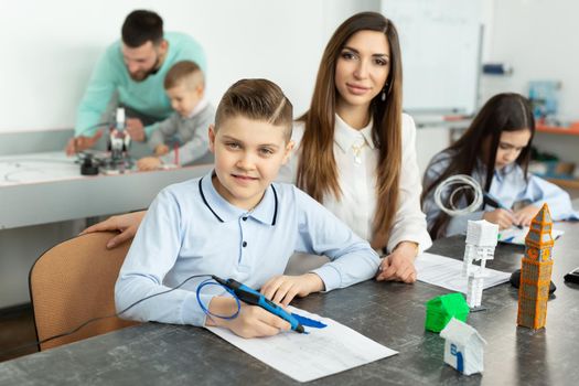 Lesson in the robotics hall. Mom and son use a pen for 3D printing.