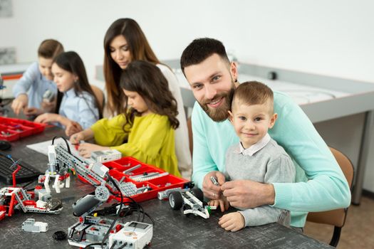 Family with children in a robotics club makes a robot controlled from a constructor.