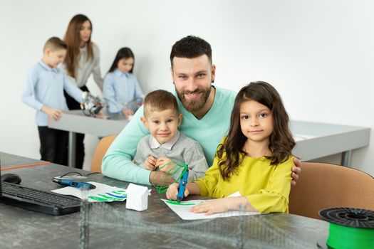 Young father with his son and daughter draw a drawing using a 3D pen in robotics classes