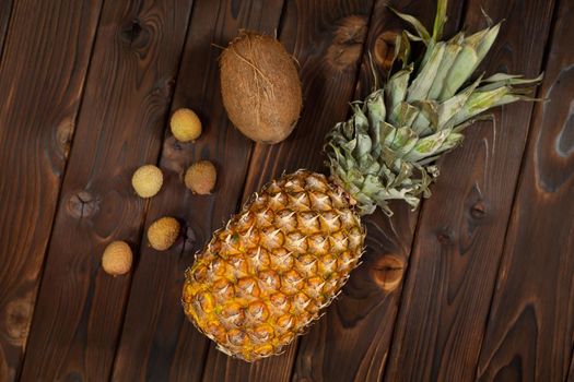 Exotic fruits: pineapple, coconut and lychee on a brown wooden background.