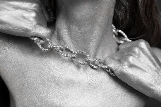 Beautiful woman with silver paint on her skin and hair breaks the chain around her neck.