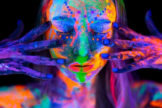 Beautiful young woman in neon light. Portrait of a model with fluorescent makeup posing in UV light with colorful makeup