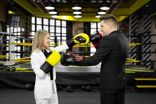 Picture of a businessman and a businesswoman sparring with boxing gloves against of a boxing ring.