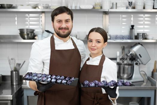 Couple of loving confectioners, a man and a woman, embrace and hold a chocolate cake decor in their hands.