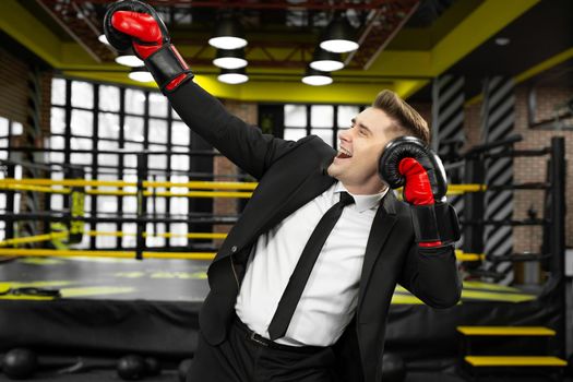 Young male businessman in a suit and boxing gloves is having fun and laughing.