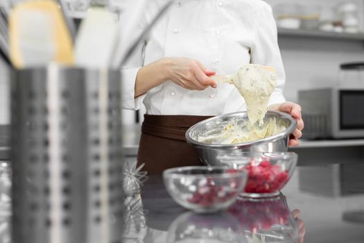 Pastry chef kneads the dough for making a cake