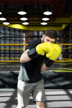 The assembled athlete in the boxing gym practices boxing punches during training and looks at the camera