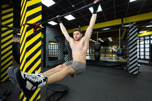 Young man flexing abdominal muscles on pull-up bar in gym