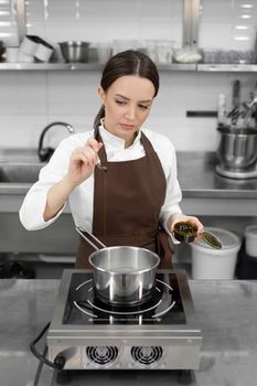 Young female pastry chef adds pistachio paste to the boiling syrup. Cooking dessert in a professional kitchen