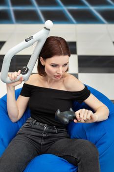 An emotional woman sits in a chair and plays video games console VR with an controller.