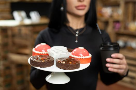 Coffee in a cardboard cup and desserts on a tray close-up in the hands of a woman.