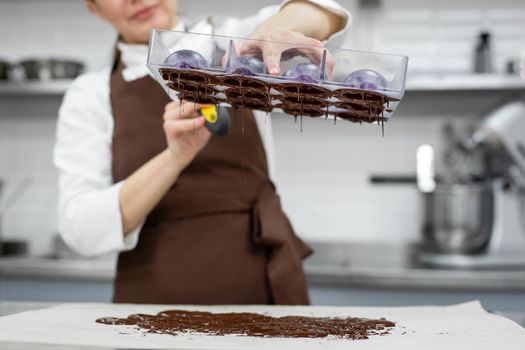 Chef or chocolatier makes sweet chocolates in a professional kitchen. She turns the mold over and pours the rest of the chocolate onto the table.