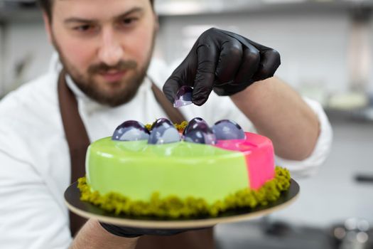 Young smiling chef decorates a mousse cake with handmade chocolates.