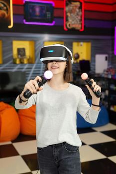 Child, a teenage girl playing on a game console in virtual reality glasses shooting a game with a remote control gun in a game club. VR