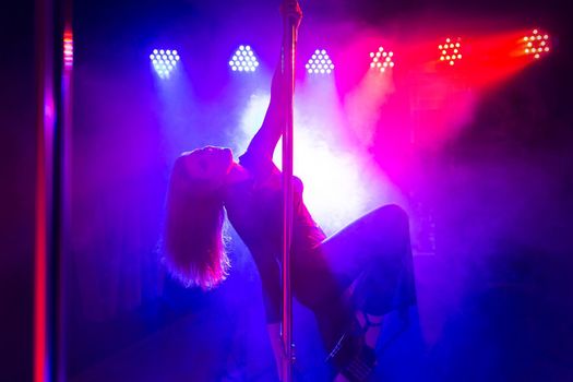 Pole dance. Young slender sexy woman dancing on a pole in the interior of a nightclub with light and smoke.