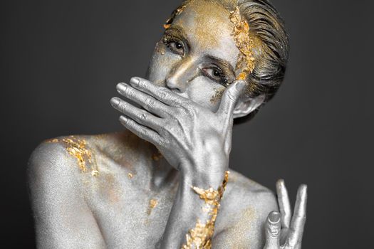 Portrait of a beautiful female model with gold and silver paint on her skin and hair in the studio.