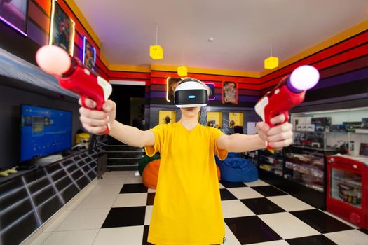 Teen, baby boy playing on a video game console, emotional gamer shooting a game using a gun controller in a game club. VR