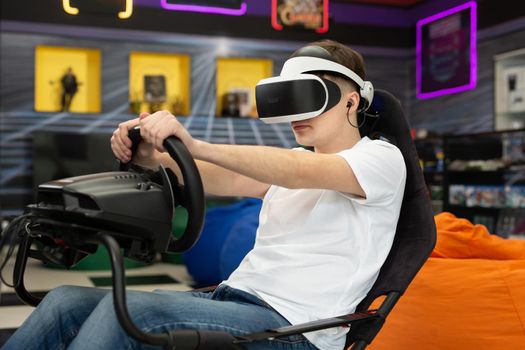 Teenage boy wearing virtual reality glasses, who holds on to the steering wheel and plays a computer game on the console