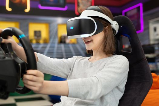 Teenage girl wearing virtual reality glasses, who holds on to the steering wheel and plays a computer game on the console