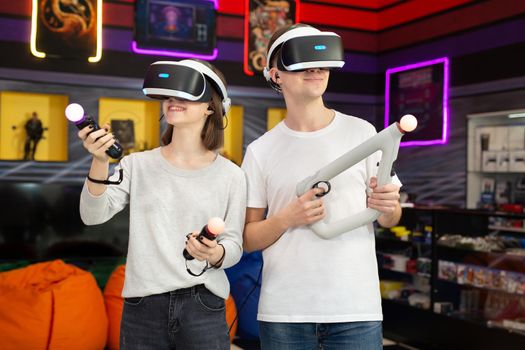 Portrait of teenagers, a boy and a girl with a virtual reality headset in glasses and hand movement controllers in a game club.