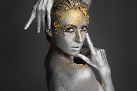 Portrait of a beautiful female model with gold and silver paint on her skin and hair in the studio.