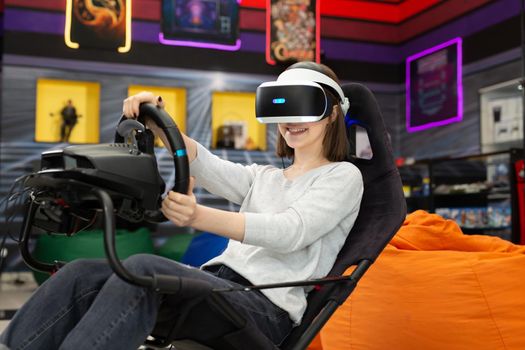 Teenage girl wearing virtual reality glasses, who holds on to the steering wheel and plays a computer game on the console