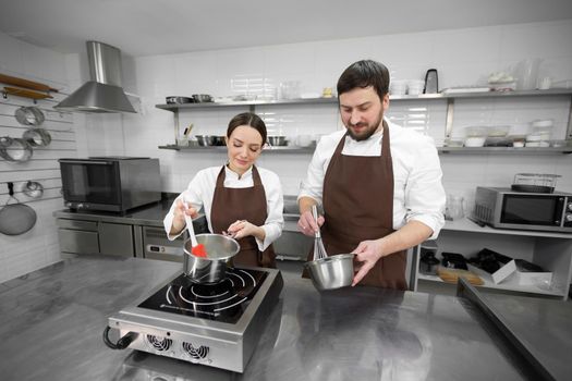 Man and woman confectioners prepare dessert together in a professional kitchen, cook syrup and cream.