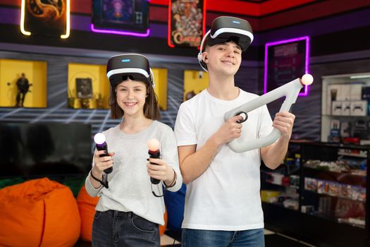 Portrait of teenagers, a boy and a girl with a virtual reality headset in glasses and hand movement controllers in a game club.