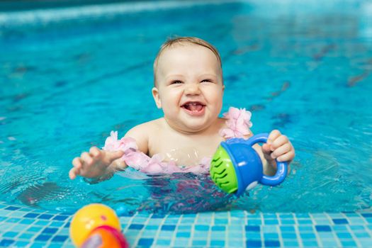 Little baby girl is playing with bright toys in the pool.