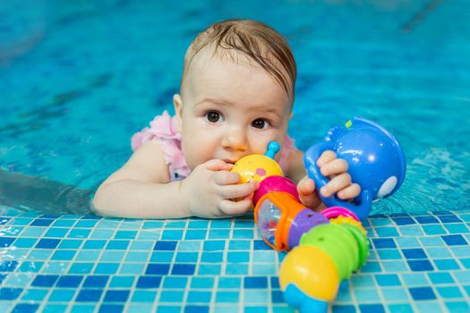 Little baby girl is playing with bright toys in the pool.