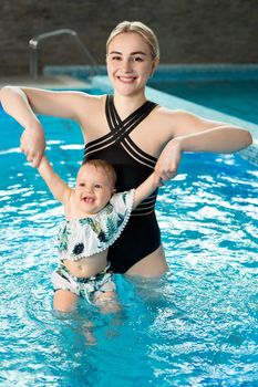 Young mother, swimming instructor and happy little girl in the pool. Teaches infant child to swim.