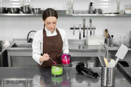 Female pastry chef paints a mirror glaze in green and pink in a professional kitchen.