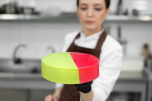 Young smiling brunette chef holds a mousse cake decorated with handmade chocolates.