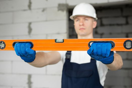 Smiling man is a worker or construction worker wearing a helmet with a level on the background of a brick wall.