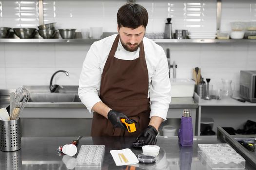 Male pastry chef measures the temperature of the chocolate glaze with a non-contact thermometer in a professional kitchen.