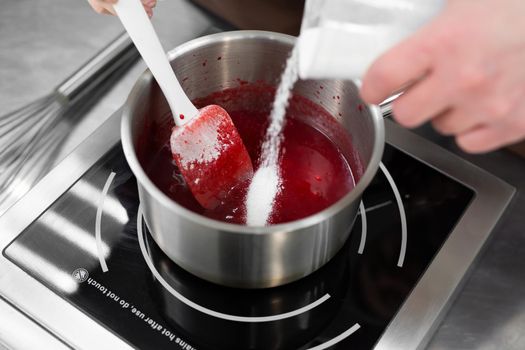 Close-up of the hands of a man and a woman-confectioners prepare berry filling for a cake, mix and add sugar to the syrup.