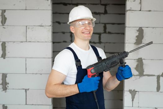 Construction worker in a white helmet is holding an electric drill. Professional tools.