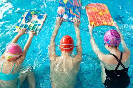 Group of boys and girls train and learn to swim in the pool with an instructor. Development of children's sports.