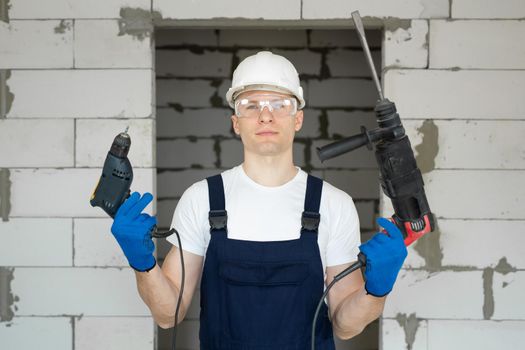 Professional construction worker in a white hard hat is holding a drill and a screwdriver.