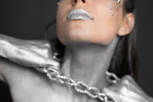 Beautiful woman with silver paint on her skin and hair breaks the chain around her neck.