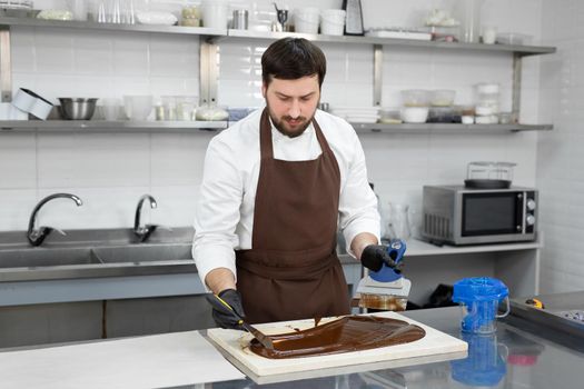 Male chocolatier uses a spatula to stir the tempered liquid chocolate on a granite table