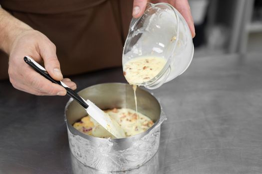 Close-up of a female pastry chef's hands pouring mousse into a mold.