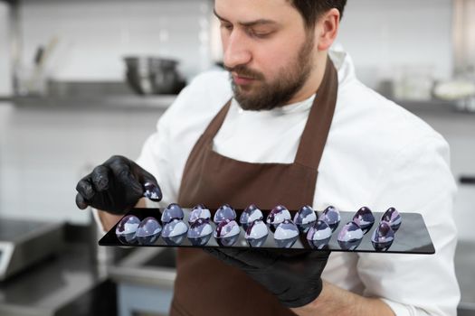 Close-up of the hand of a male pastry chef-a man laying out colored chocolates on a black mirror surface.