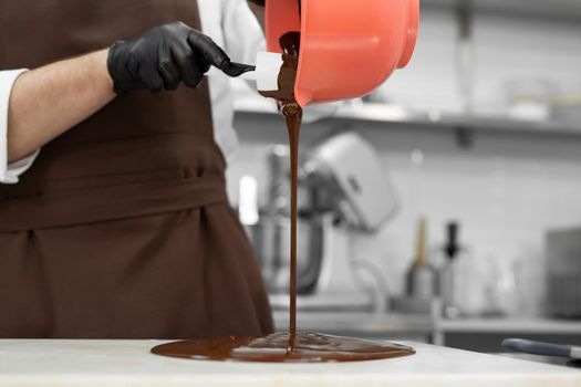 Male chocolatier pours melted chocolate onto a granite table.