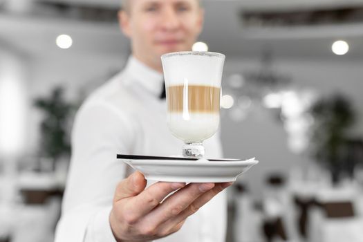 Close-up of a latte in the hands of a male waiter.