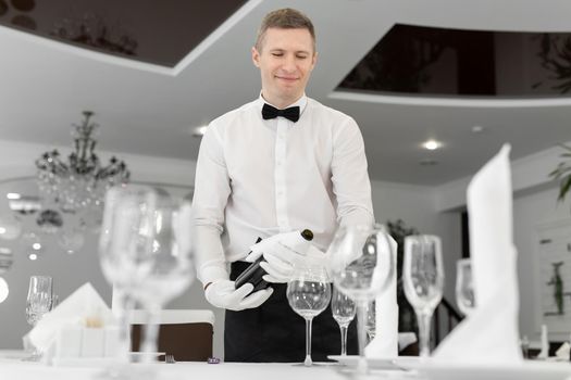 Male waiter in white gloves pours red wine into a glass.