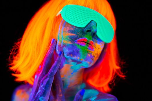 Beautiful model woman in wig and glasses with colorful bright fluorescent makeup in neon light, nightclub disco.